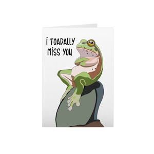 May include: A greeting card with a green frog sitting on a rock. The card says "i toadally miss you".
