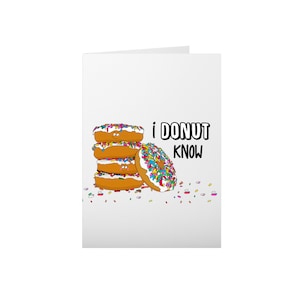 May include: A white card with a stack of four donuts with colorful sprinkles and a white frosting. The donuts have smiley faces. The text "i DONUT KNOW" is written in black letters.