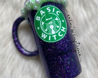May include: A purple glitter tumbler with a green and white logo that says "Basic Witch" and a witch wearing a hat. The tumbler has a white rim and a green liquid with white bubbles.