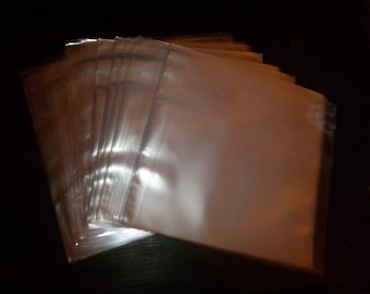 May include: A stack of clear, transparent plastic sleeves, likely for protecting documents or photos. The sleeves are rectangular and appear to be made of a thin, glossy material. The image is taken in low light, with the sleeves fanned out.