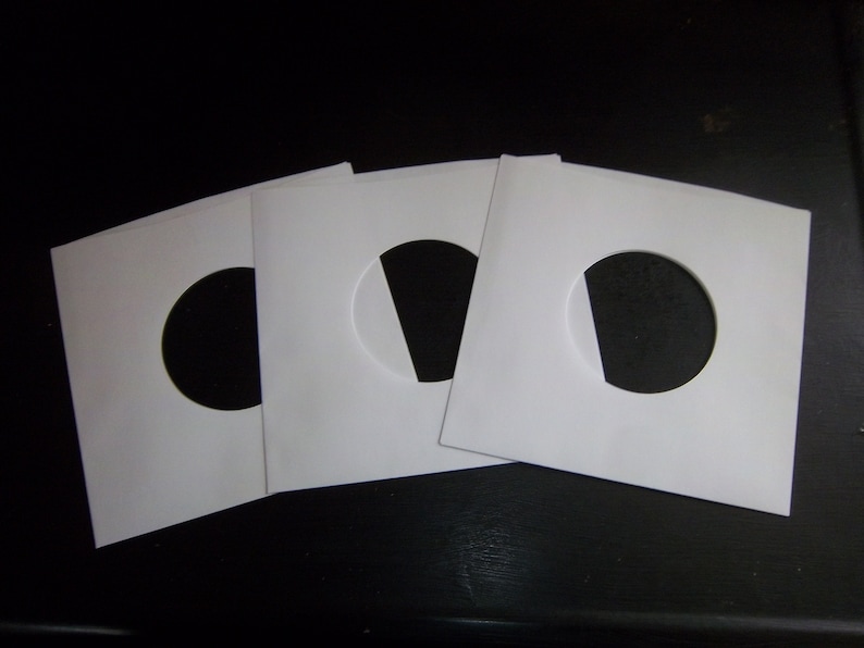 May include: Three white paper record sleeves with a round hole in the center. The sleeves are designed to protect vinyl records.