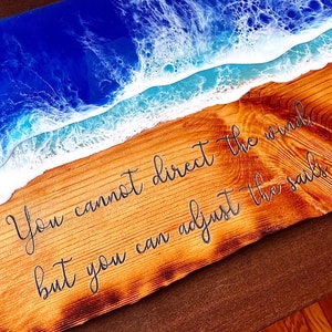 May include: A wooden sign with a blue and white epoxy resin wave design. The sign has the quote "You cannot direct the wind, but you can adjust the sails" written on it.