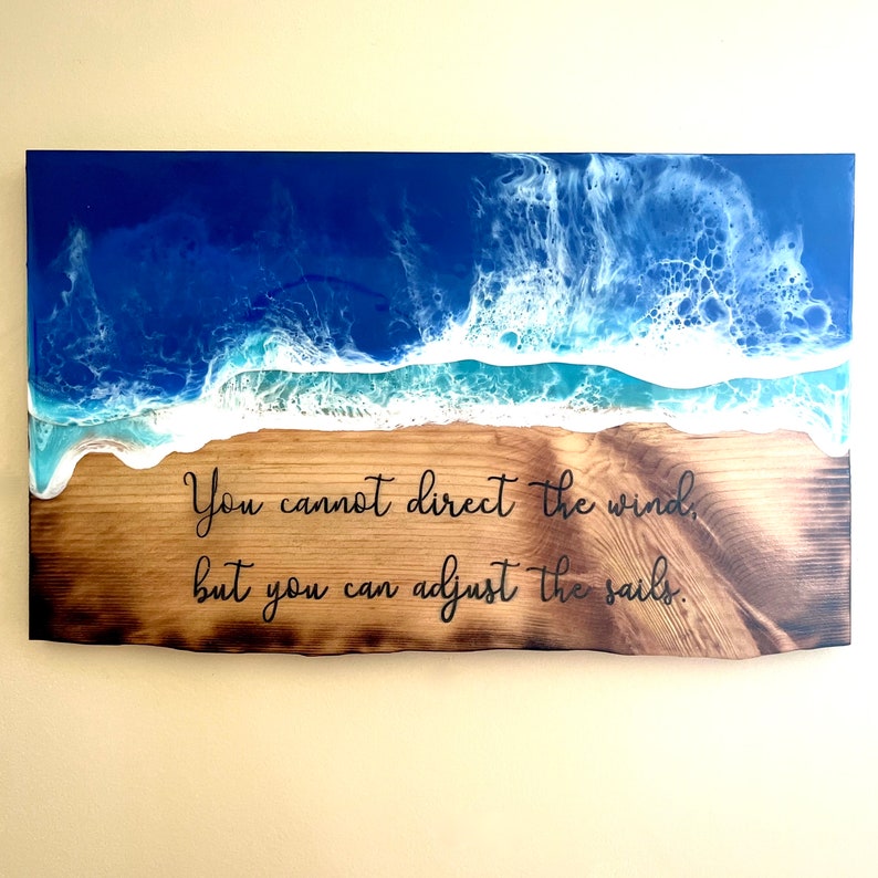 May include: A wooden sign with a blue and white epoxy resin ocean wave design. The sign has the quote "You cannot direct the wind, but you can adjust the sails."  burned into the wood.