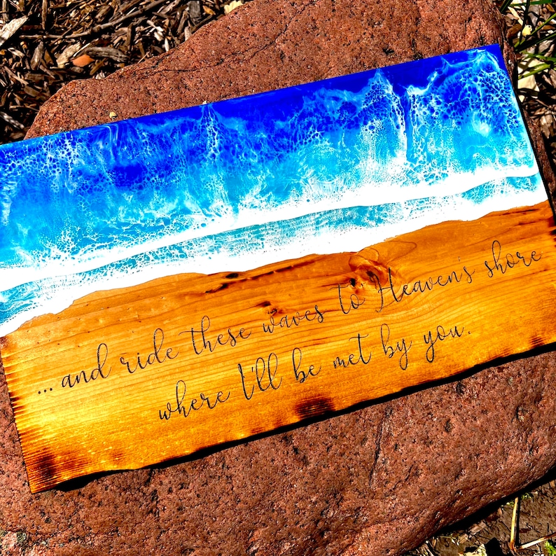 May include: A wooden sign with a blue and white epoxy resin ocean wave design. The sign has the text "...and ride these waves to Heaven's shore where I'll be met by you."