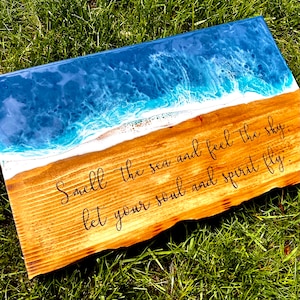 May include: A wooden sign with a blue and white epoxy resin ocean wave design. The sign has the text "Smell the sea and feel the sky, let your soul and spirit fly."