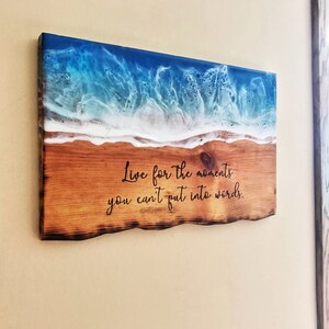 May include: Wooden wall art with a blue and white resin ocean wave design. The wood has a rustic, burnt look. The quote "Live for the moments you can't put into words." is inscribed on the wood.