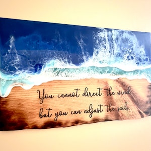 May include: A wooden sign with a blue and white resin ocean wave design. The sign has the quote "You cannot direct the wind, but you can adjust the sails." burned into the wood.