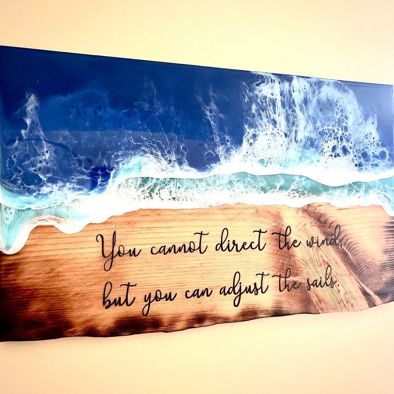May include: A wooden sign with a blue and white resin ocean wave design. The sign has the quote "You cannot direct the wind, but you can adjust the sails." burned into the wood.
