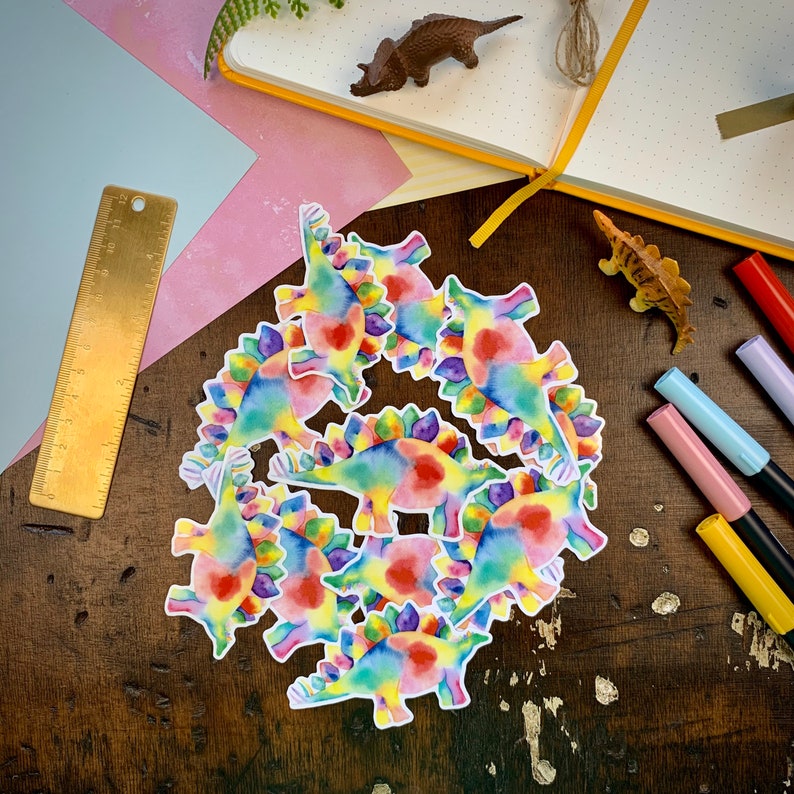 May include: A set of ten colorful dinosaur stickers with rainbow-colored scales. The stickers are perfect for adding a fun and whimsical touch to any project.