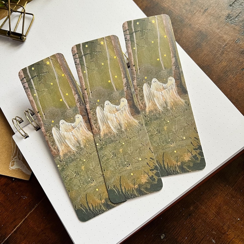 May include: Three bookmarks featuring a forest scene with glowing lights and white ghosts. The bookmarks are printed on a textured paper with a green and brown background.