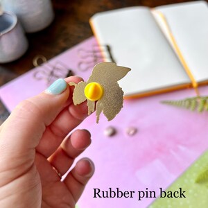 May include: Gold-colored metal bee pin with a yellow rubber pin back. The bee is in a dripping honey design.