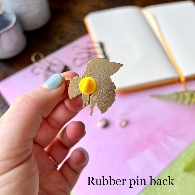 May include: Gold-colored metal bee pin with a yellow rubber pin back. The bee is in a dripping honey design.