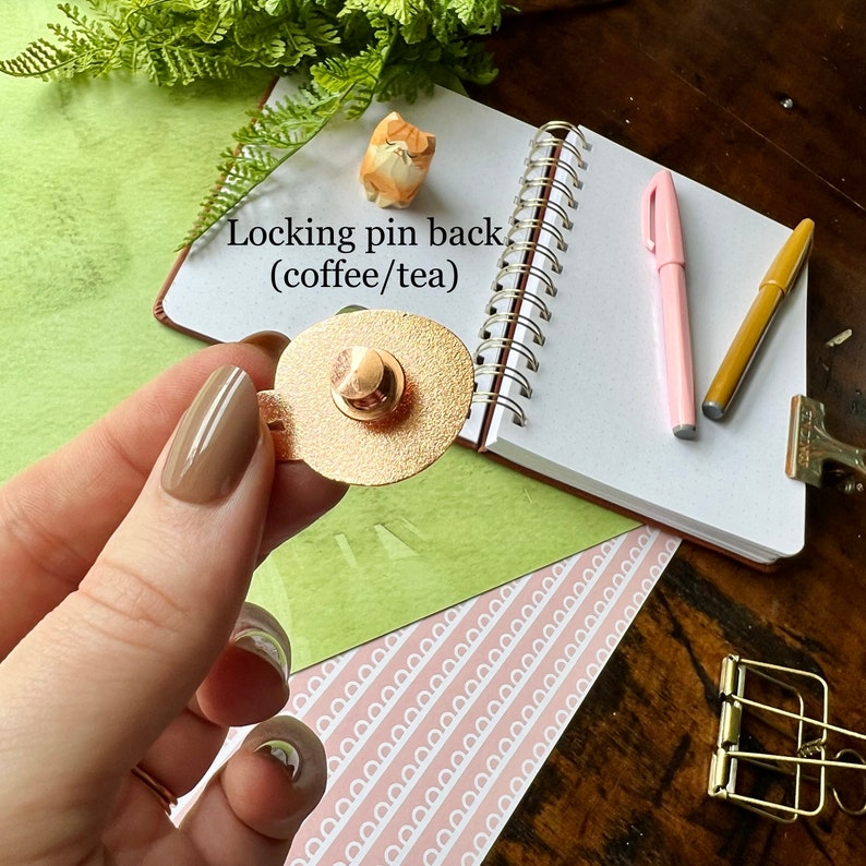 May include: A gold-colored locking pin back for a brooch or pin. The pin back is oval-shaped and has a textured surface. The text "Locking pin back (coffee/tea)" is visible in the image.