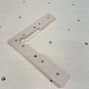 May include: A light brown wooden corner brace with multiple holes drilled into it. The brace is designed to be used in woodworking projects.