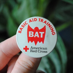 May include: White button with red text and a red graphic. The text reads "Basic Aid Training BAT American Red Cross".