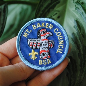 May include: A blue and yellow embroidered patch with the text "Mt. Baker Council BSA" and a stylized totem pole design.
