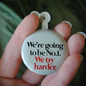 May include: White button with black text that reads "We're going to be No.1. We try harder."