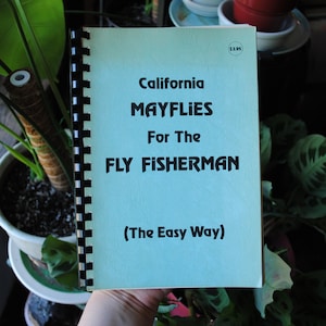 Puede incluir: Un libro azul con el título "California Mayflies For The Fly Fisherman (The Easy Way)" en la portada. El libro está encuadernado en espiral y tiene una etiqueta de precio de $ 1,95.