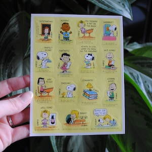 May include: A sheet of 16 colorful stickers featuring Peanuts characters with encouraging messages like "Outstanding!" and "Super Job Way To Go!"