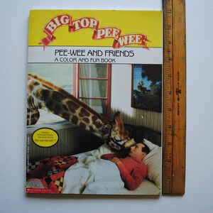 May include: A yellow and red book cover with the title "Big Top Pee-wee" and the subtitle "Pee-wee and Friends A Color and Fun Book". The cover features a giraffe reaching down to a man lying in bed.