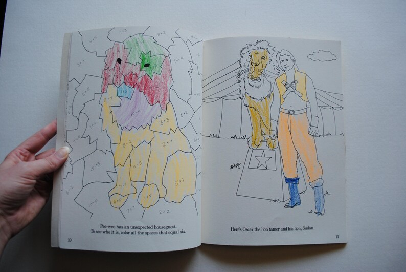 May include: A coloring book page with a lion and a person. The lion is standing on a pedestal with a star on it. The person is standing next to the lion and has a star on their chest. The text on the page says "Here's Oscar the lion tamer and his lion, Sheldon."