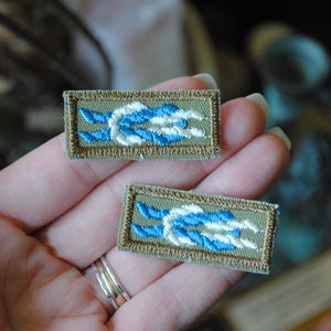 May include: Two embroidered patches with a blue and white rope design on a khaki background.