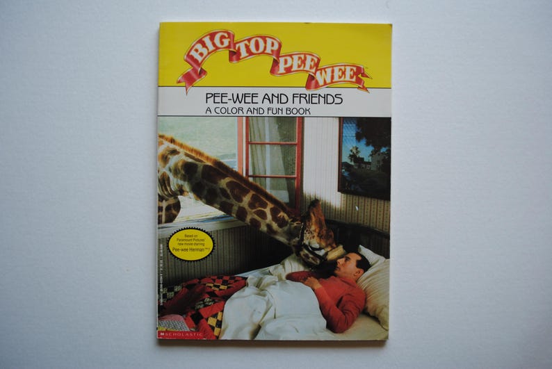 May include: A yellow and red book cover with the title "Big Top Pee-wee" and the text "Pee-wee and Friends A Color and Fun Book". The cover features a giraffe with a man lying on a bed in the background.