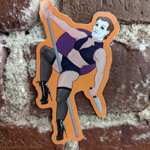 May include: An orange sticker featuring a cartoon illustration of a figure in a black lingerie set, holding a knife and a pole. The figure is wearing black high-heeled boots and a white mask. A purple circle is behind the figure.