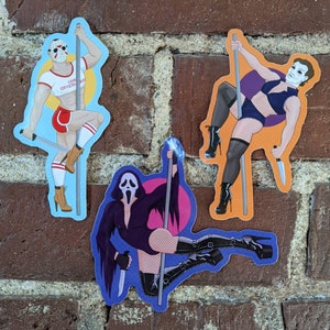 May include: Three die-cut stickers featuring horror movie characters in provocative poses. One sticker depicts a figure in a hockey mask, holding a knife and wearing a white top and red shorts. Another shows a figure in a white mask, holding a knife and wearing a black robe. The third shows a figure in a mask, holding a knife and wearing a blue outfit.