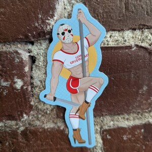 May include: A sticker featuring a muscular figure wearing a hockey mask, red shorts, and a white crop top with the text "Camp Crystal Lake." The figure is holding a pole and a machete, with brown boots and white socks.