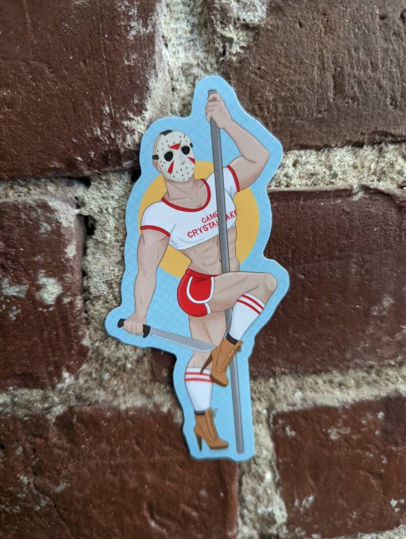May include: A sticker featuring a muscular figure wearing a hockey mask, red shorts, and a white crop top with the text "Camp Crystal Lake." The figure is holding a pole and a machete, with brown boots and white socks.