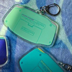 May include: A green and yellow Game Boy Advance keychain with the text "PISS BOY ADVANCE" and "MAN IN CHHEUS CAN TREZMAS FST IN URMUTH PUVAD BU CANT BELIEVE U FELL FOR THAT" printed on it.