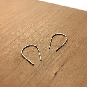 May include: A pair of gold-toned hoop earrings with a simple, minimalist design. The earrings are made of thin wire and have a slightly curved shape.