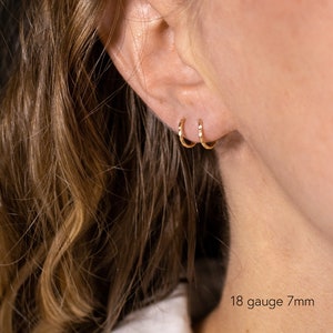 May include: Close-up of a person's ear with two gold hoop earrings. The earrings are 7mm in diameter and 18 gauge.