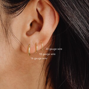 May include: Close-up of a person's ear with three gold hoop earrings of different sizes. The earrings are labeled with their gauge size: 16 gauge, 18 gauge, and 20 gauge.