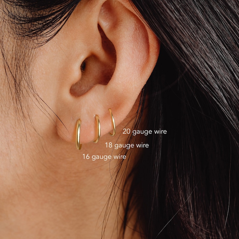 May include: Close-up of a person's ear with three gold hoop earrings of different sizes. The earrings are labeled with their gauge size: 16 gauge, 18 gauge, and 20 gauge.