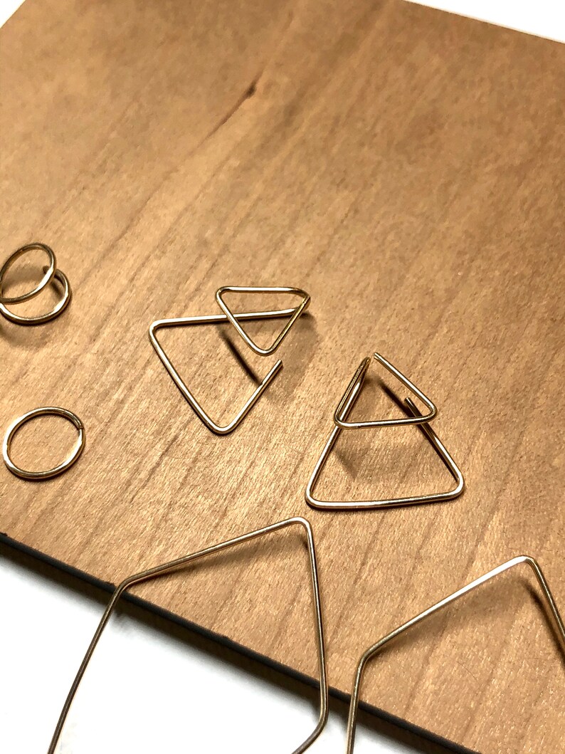 K&ouml;nnte beinhalten: Ein Set goldener geometrischer Ohrringe mit einem Paar Doppel-Dreiecks-Ohrringen und einem Paar quadratischen Creolen.