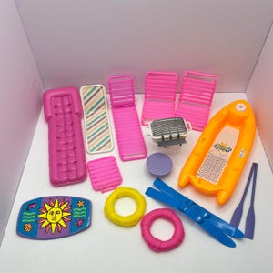May include: A collection of plastic doll-sized camping and beach accessories including a pink air mattress, three pink lounge chairs, a small grill, a yellow inflatable boat with a CAMP decal, two oars, two life rings, and a sun-themed board.