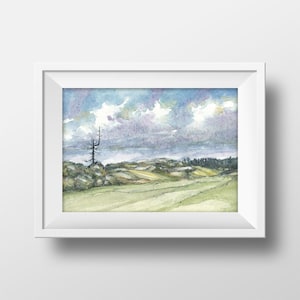 May include: Framed watercolour landscape print. The artwork shows a field with rolling hills beneath a cloudy sky. The colour palette features greens, blues, and purples, creating a tranquil, natural scene.