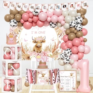 May include: A festive first birthday party setup with a cow theme. Includes a balloon arch in pink, brown, and white, a backdrop with a cow illustration, and a cake. The setup also features a "ONE" balloon and a "First Year" sign.