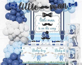 Könnte beinhalten: Babyparty-Dekoration in Blau-, Weiß- und Grautönen. Die Szene umfasst Luftballons, ein Banner mit der Aufschrift "little man" und einen Tisch mit dem Thema "Baby Boy". Die Dekorationen umfassen einen Kuchen, Cupcakes und Boxen mit der Aufschrift "BABY".