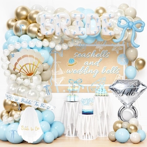 May include: A balloon arch featuring gold, white, and light blue balloons with a large blue bow, a shell-shaped balloon, and a diamond ring balloon. A banner reads Bride To Be, and a sign displays seashells and wedding bells with a veil below.