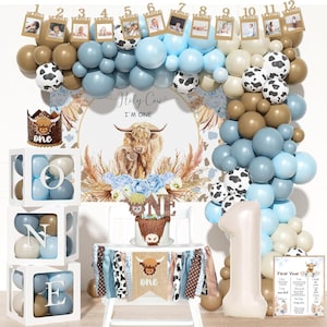 May include: A festive first birthday party setup with a cow theme. Includes a balloon arch in blue, brown, and white, a cake, and decorations. The backdrop reads "Holy Cow, I'm One."