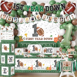 May include: A football-themed first birthday party decoration set. Includes balloons, banners, tableware, and decorative blocks. The color scheme features green, brown, and white, with football and field graphics. The banner reads "1st Year Down."