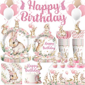 May include: A collection of pink and white birthday party decorations featuring a bunny theme. Includes plates, cups, napkins, a banner that says "Happy Birthday", balloons, and cake toppers. The decorations have floral and bunny designs.