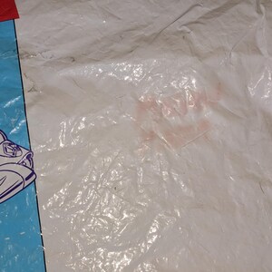 May include: A white plastic bag featuring a graphic of the character Buzz Lightyear from Toy Story. The character is depicted in a white, purple, and green space suit on a light blue background. The top left corner shows part of the red Toy Story logo.