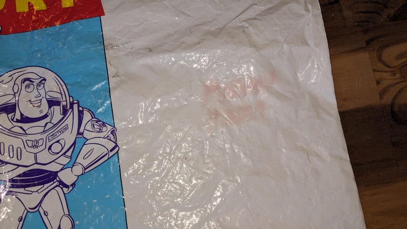 May include: A white plastic bag featuring a graphic of the character Buzz Lightyear from Toy Story. The character is depicted in a white, purple, and green space suit on a light blue background. The top left corner shows part of the red Toy Story logo.