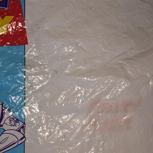 May include: A white plastic bag featuring a partial blue border on the left side. The visible graphic includes a red square with a yellow letter Y and a portion of a white and blue character illustration. The plastic surface is wrinkled and creased.