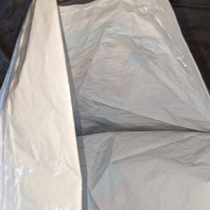 May include: A white plastic shipping mailer bag with a smooth, opaque surface and a rectangular shape. The bag is partially open at the top, revealing the interior space. The material is flexible, lightweight, and features a clean, plain exterior.