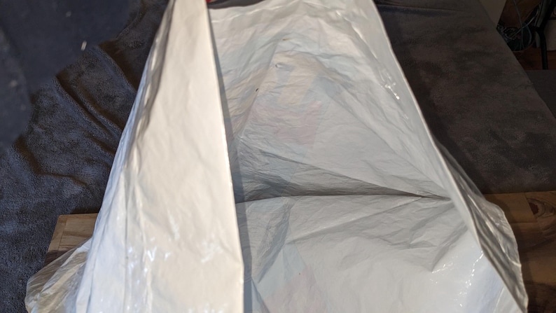 May include: A white plastic shipping mailer bag with a smooth, opaque surface and a rectangular shape. The bag is partially open at the top, revealing the interior space. The material is flexible, lightweight, and features a clean, plain exterior.